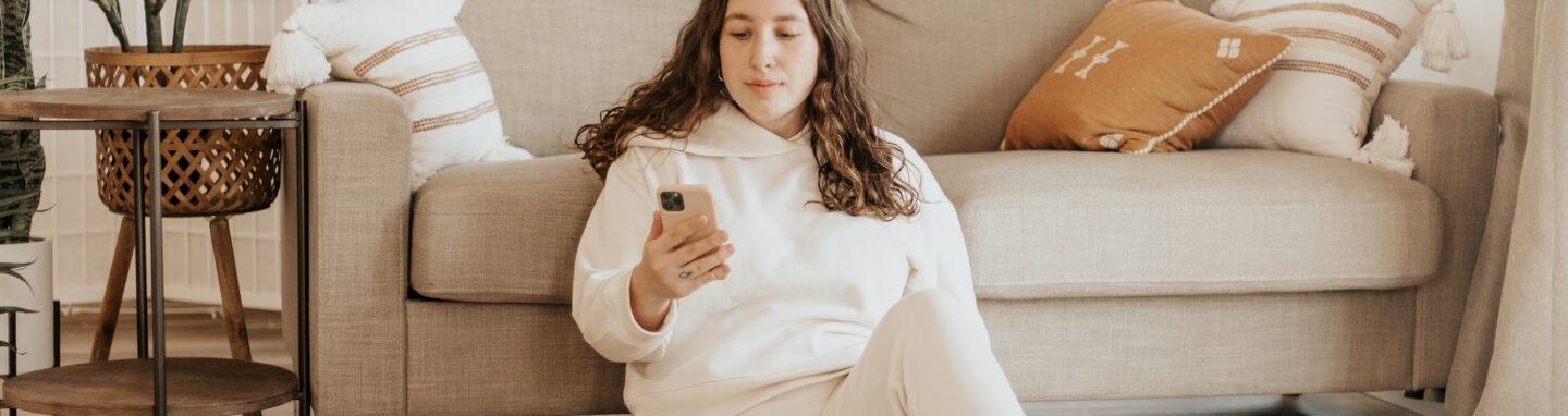 Frau sitzt neben Couch mit Handy