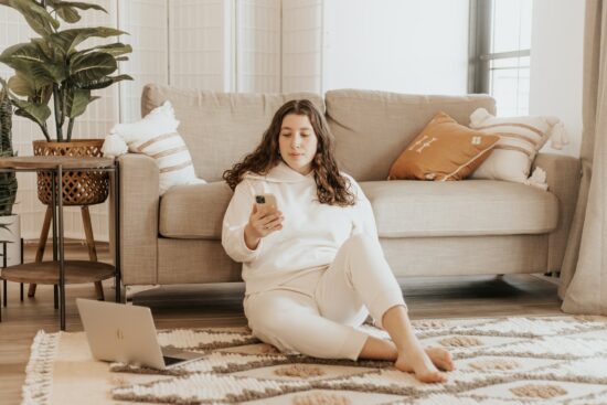 Frau sitzt neben Couch mit Handy