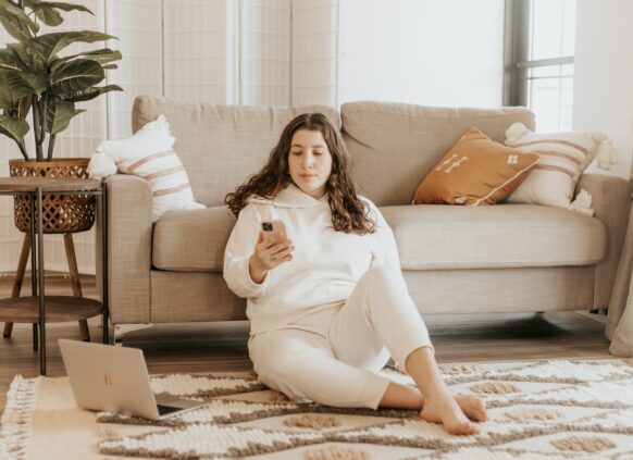 Frau sitzt neben Couch mit Handy