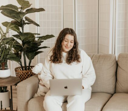 Junge Frau sitzt auf dem Sofa und schaut auf ihr Laptop