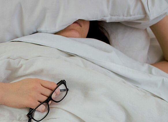 Frau liegt erschöpft im Bett mit Brille in der Hand