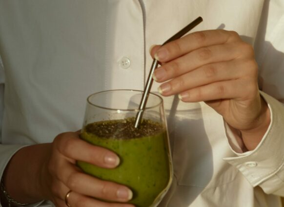 Frau in weißer Bluse hält ein Glas mit einem grünen Smoothie