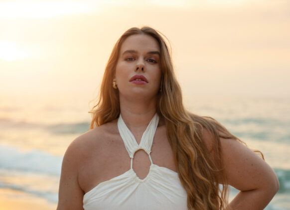 Eine selbstbewusste Frau in einem weißen Sommerkleid posiert am Strand.