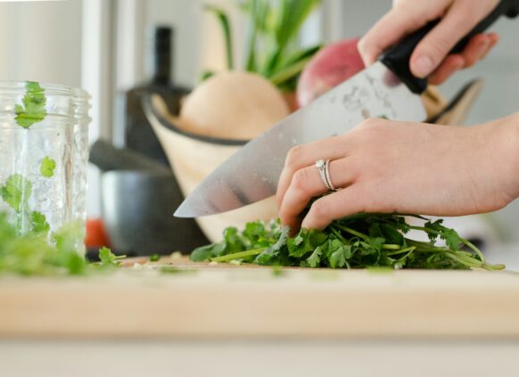 Ein Ausschnitt, auf dem eine Frauenhand zu sehen ist, die mit einem Messer gesunde Kräuter schneidet.