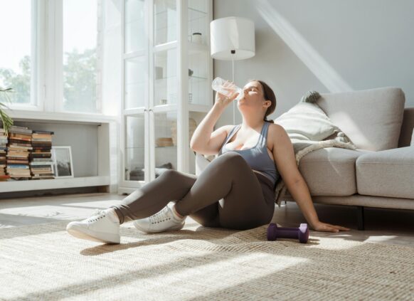 Frau sitzt auf dem Boden in Sportklamotten und trinkt wasser