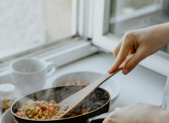 Eine Pfanne mit gekochten Gemüse wird über einen Teller gehalten, um das Essen darauf zu tun.