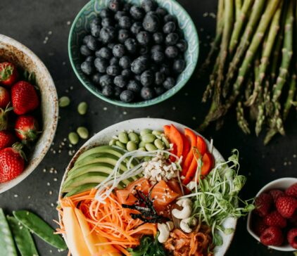 Bowl mit Avocado, Lachs und weiterem Gemüse auf einer dunklen Platte mit Obst