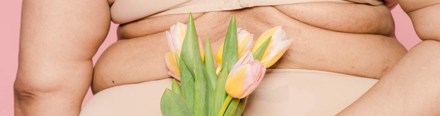 Kurven einer Frau im Hüftbereich. Eine Hand hält mit Tulpen davor.