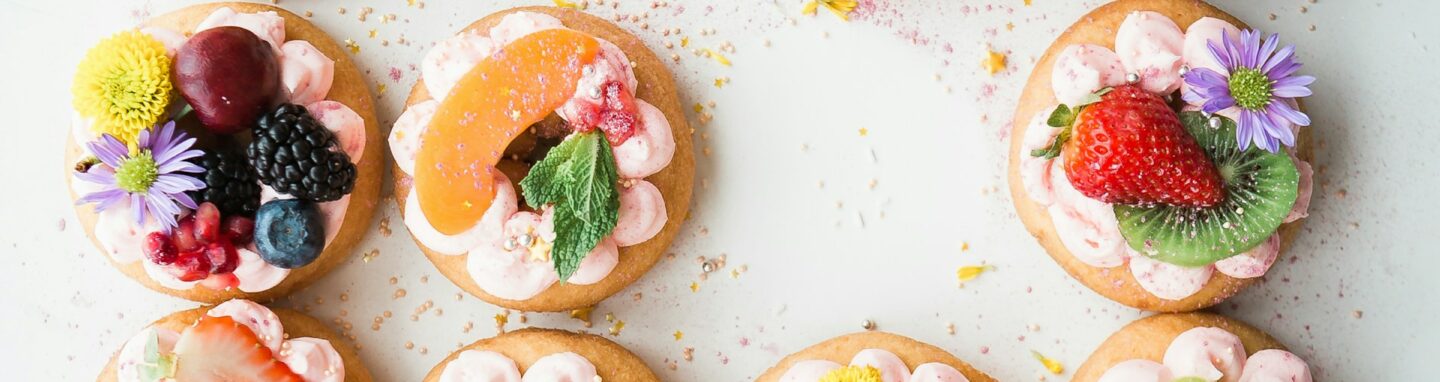 Platte mit kleinen Donouts, auf denen Früchte garniert sind.