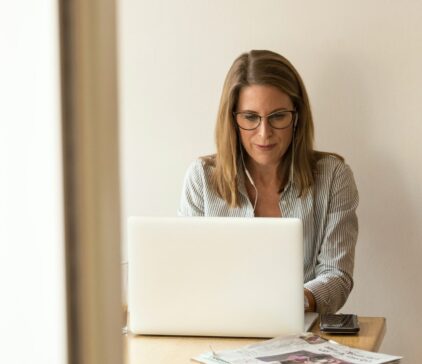 Frau mit Brille sitzt an einem Tisch vor ihrem Laptop