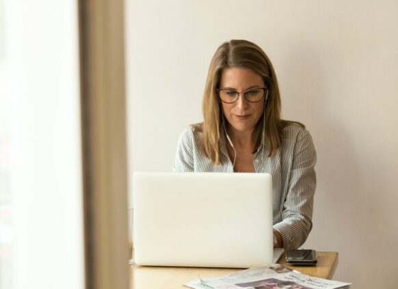 Frau mit Brille sitzt an einem Tisch vor ihrem Laptop