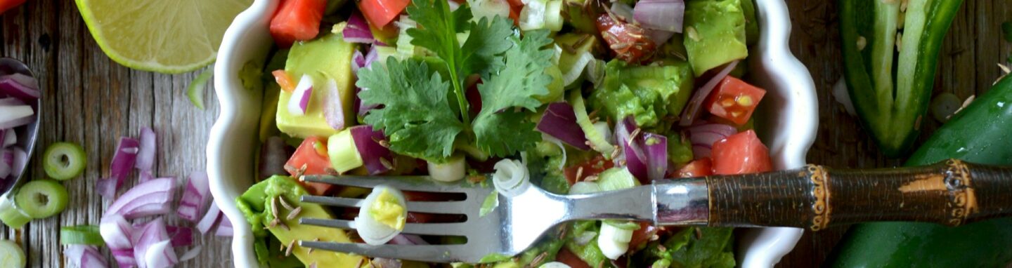 Teller mit buntem Salat auf einer Holzplatte umgeben von verschiedenen Gemüse Sorten