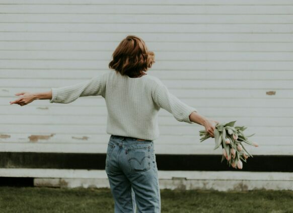 Frau mit Blumen in der Hand hat ihre Arme ausgebreitet und dreht sich.