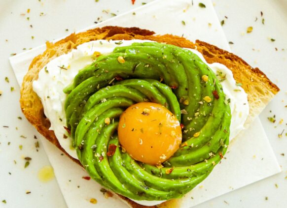 Eine halbe Scheibe Brot mit Avocado Streifen und einem Eigelb.
