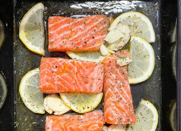 Einige Stücke Lachsfilet auf Zitronenscheiben auf einem Blech garniert.
