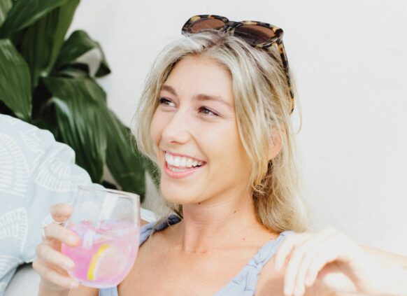 Eine junge lachende Frau hält ein Glas Limonade in der Hand.