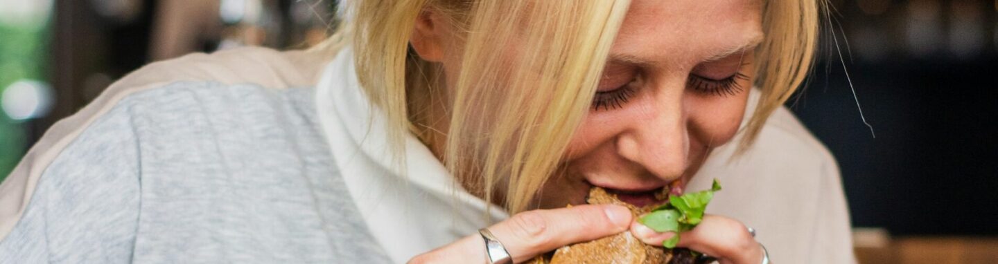 Frau isst einen Burger und vor ihr auf dem Tisch iegt noch mehr Junkfood.