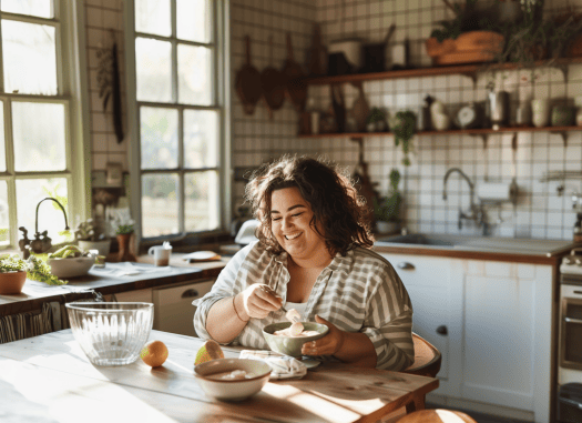 Eine plus size rau sitzt ein ihrer Küche und isst eine Joghurt Bowl.