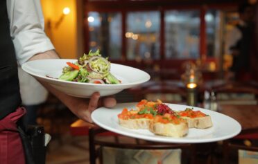 Kellner hält zwei Teller zum Abendessen,mit Salat und Bruschetta.