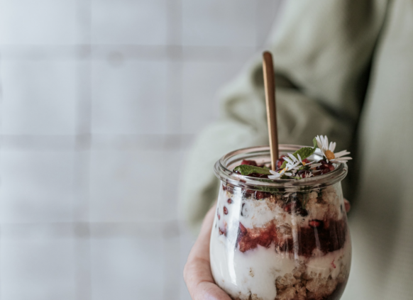 Frau hält ein Glas mit geschichtetem Chia Pudding und Früchten in der Hand