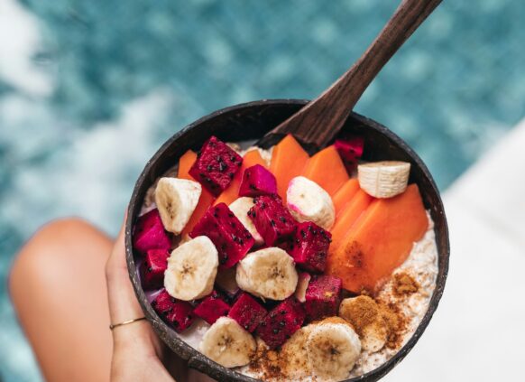 Eine Hand hält eine Porridge Bowl mit frischem Obst. Im Hintergrund sieht man einen swimming pool.