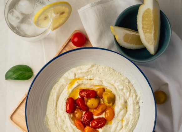 Eine Schüssel mit frischem Hummus einem Schuss Olivenöl und Tomaten.