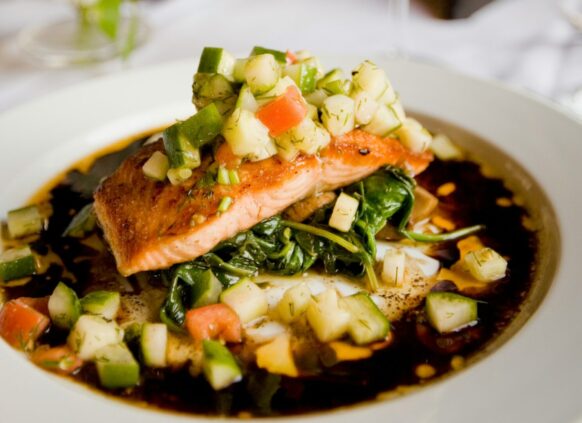 Lachs mit Gemüse und Soße auf einem Teller garniert.