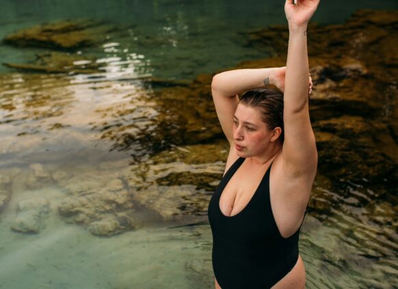 Eine selbstbewusste junge plus size Frau im Badezug stehend im einem klaren See.