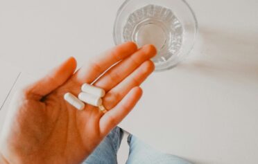 Eine Hand hält ein paar Tabletten, daneben steht ein Wasserglas.