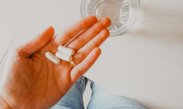 Eine Hand hält ein paar Tabletten, daneben steht ein Wasserglas.