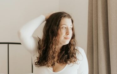 Eine junge Frau kniet auf einem Bett und blickt aus dem Fenster.