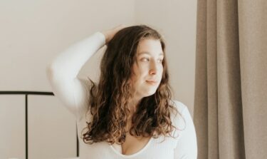 Eine junge Frau kniet auf einem Bett und blickt aus dem Fenster.