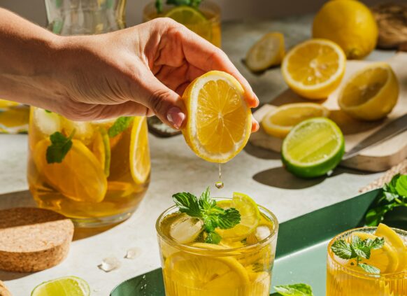 Zwei Gläser mit Zitronenlimonado, wo in ein Glas noch extra Zitronensaft gequetscht wird.