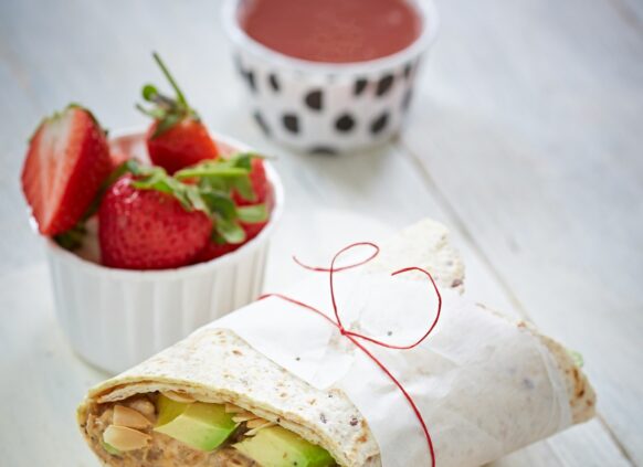 Zwei eingepackte Wraps liegen mit einer Schale Erdbeeren daneben auf einem Tablett.