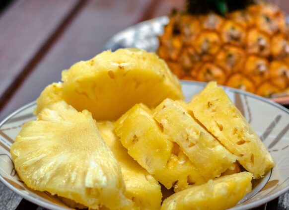 Eine Schale mit geschnittener Ananas und einer Ananasfrucht im Hintergrund.