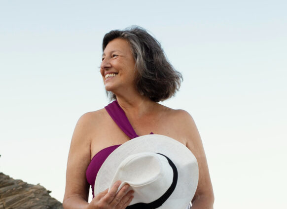 Eine ältere Dame steht am Strand und blickt zur Seite.