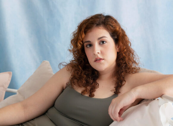 Eine junge plus size Frau sitzt im Sport set auf einem hellen Sofa.