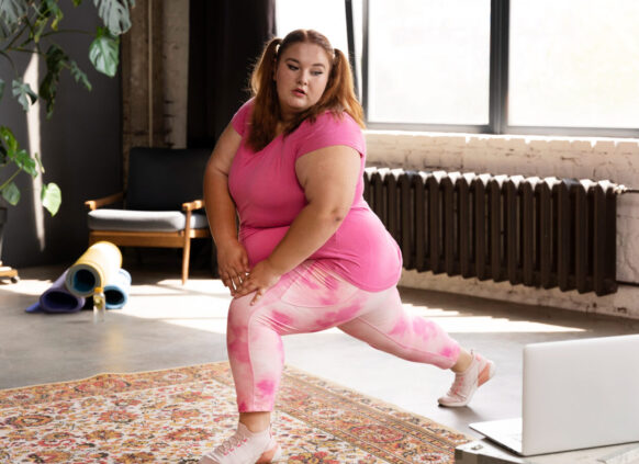 Eine junge plus size Frau macht long squats und schaut dabei auf ihren Laptop.
