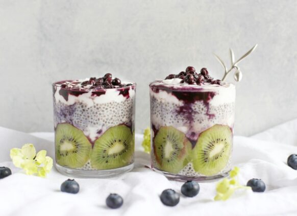 Zwei Gläser gefüllt mit Chiapudding, Kiwi und Beeren.