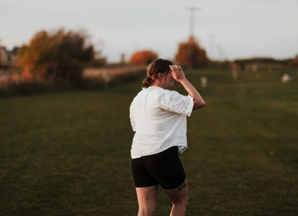 Eine plus size Frau spaziert über eine Wiese und blickt in die Ferne.