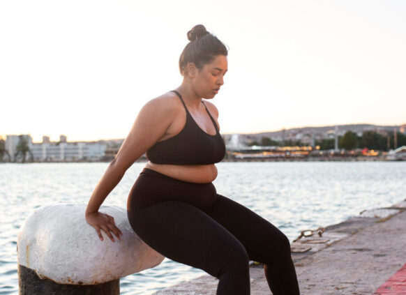 Eine kurvige Frau macht an einem Pfeiler am Hafen Sportübungen.