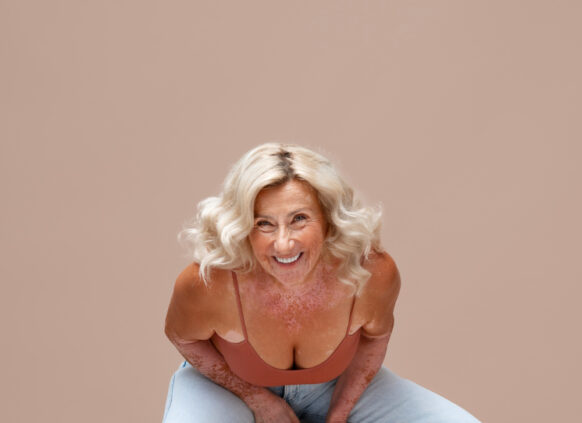 Eine altere Frau sitzt auf einem Hocker und lacht herzlich, sodass sie sich dabei nach vorne lehnt.