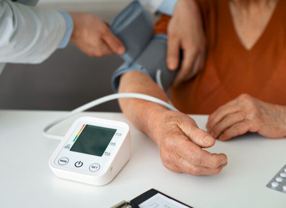 Ein Bildausschnitt, auf dem zusehen ist, wie eine medizinische Fachperson einer anderen den Blutdruck misst.