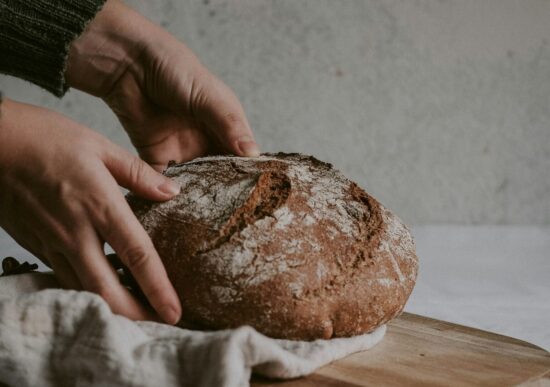 Zwei Hände nehmen einen Leib Brot von einem Holzschneidebrett.