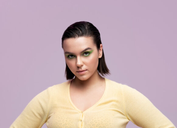 Junges curvy Model posiert selbstbewusst vor einem lila Hintergrund.