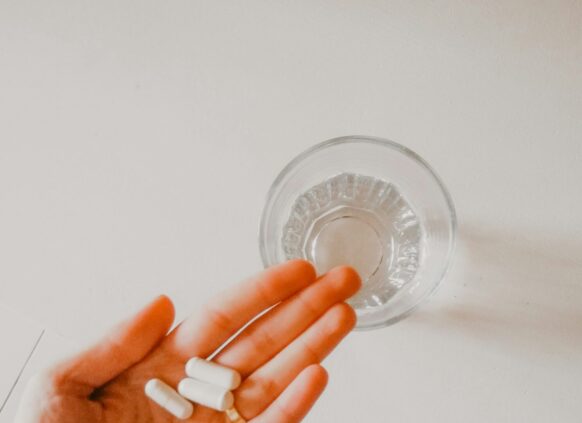 Eine Hand hält ein paar Tabletten, daneben steht ein Wasserglas.