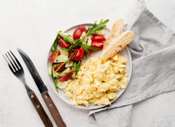 Ein Teller mit Rührei, frischem Gemüse und einer Scheibe Brot dazu.