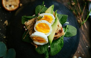 Ein Avocado-Spinat-Ei-Brot auf einem dunklen Keramik Teller.