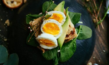 Ein Avocado-Spinat-Ei-Brot auf einem dunklen Keramik Teller.