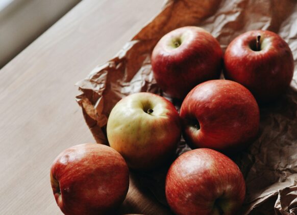 Auf einem Holzbrett liegen frische roe Äpfel, die zum Teil schon halbiert sind.